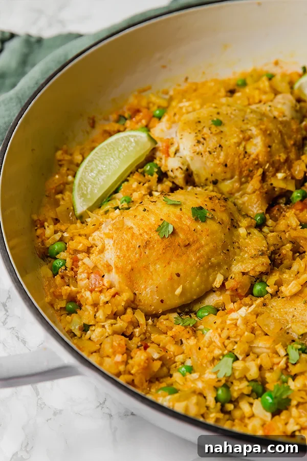 Cauliflower Arroz Con Pollo cooking in a pan, showcasing the rich colors of the chicken and vegetables.