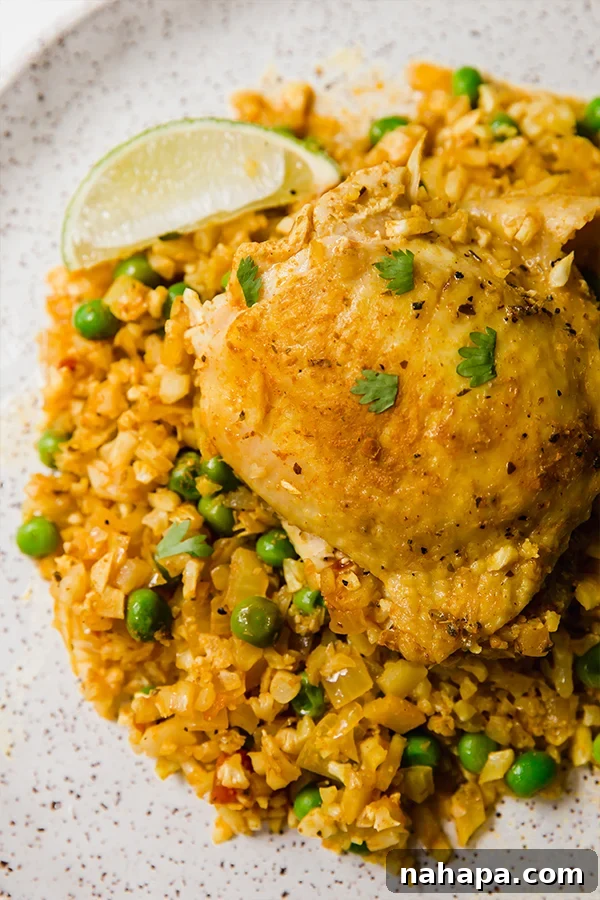 A close-up shot of the vibrant Cauliflower Arroz Con Pollo, ready to be served, topped with fresh cilantro and lime wedges.