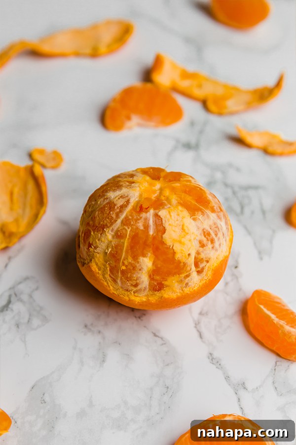 A bowl of fresh, vibrant mandarins, some with green leaves still attached, next to a cutting board.