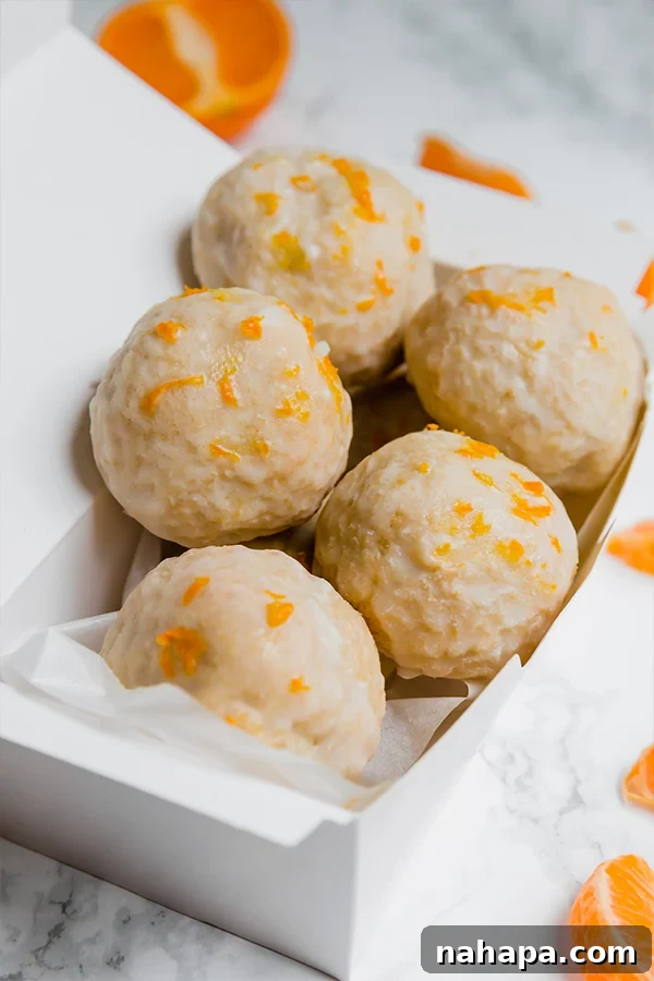 A white box filled with mandarin donut holes, some topped with extra zest, ready for serving.