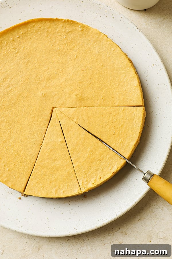 AIP Paleo Autumn Salted Caramel Pumpkin Cheesecake 5 A knife is poised to cut a slice from a whole, perfectly set dairy-free pumpkin cheesecake on a serving plate.