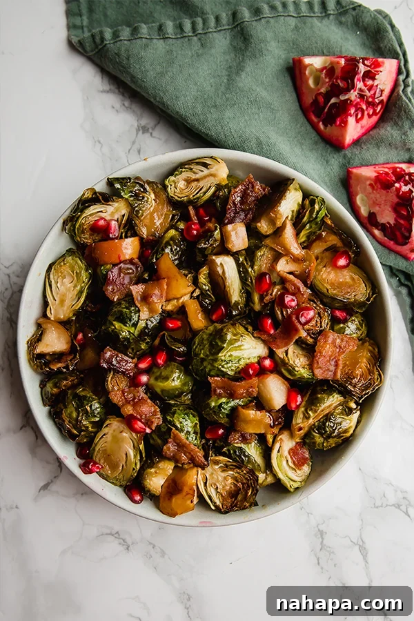 Close-up of roasted Brussels sprouts, apples, and bacon with a sprinkle of pomegranate seeds on a baking sheet.
