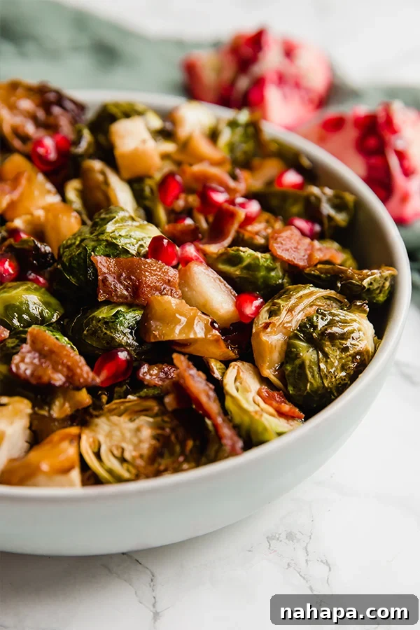 A serving of roasted Brussels sprouts, apples, and bacon with pomegranate seeds in a bowl, ready to eat.
