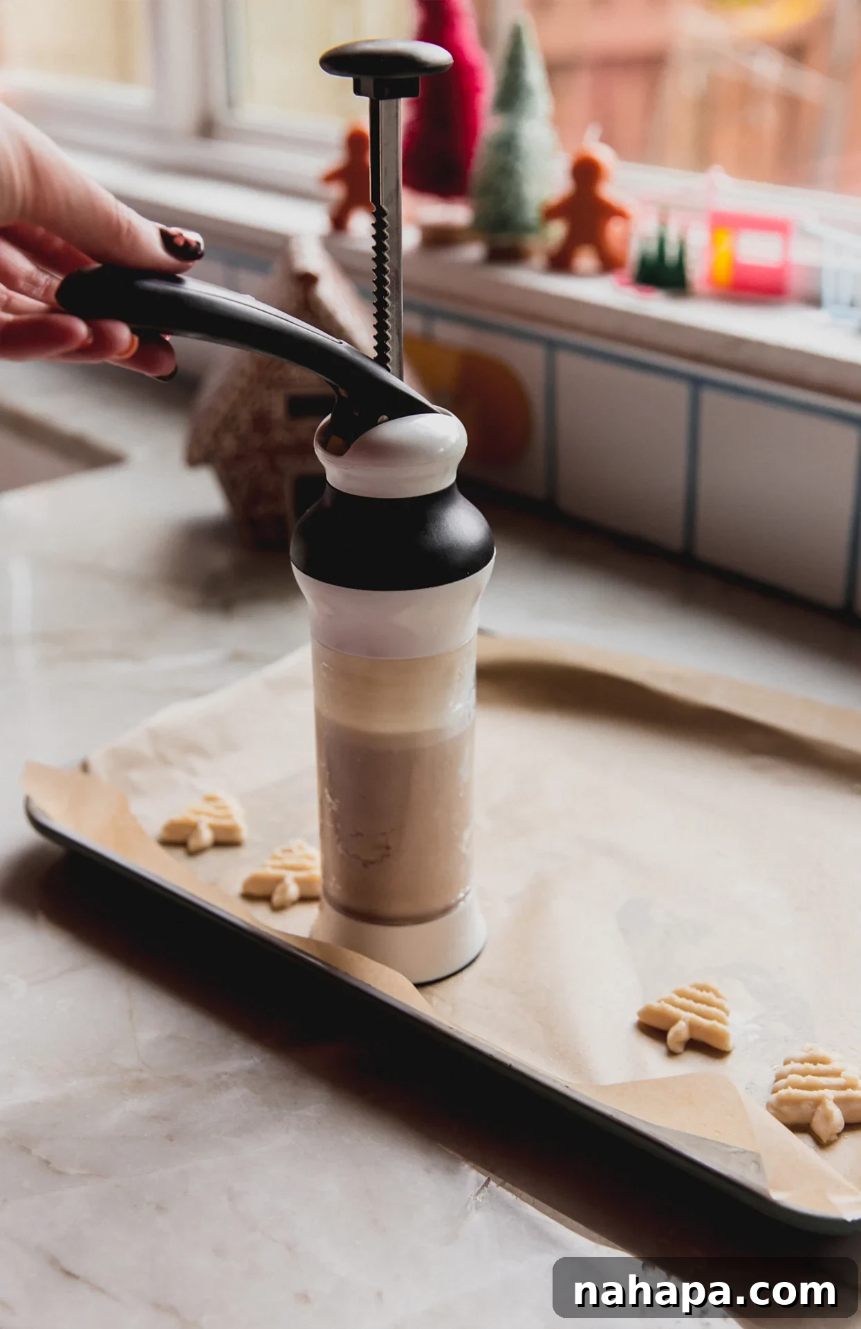 A cookie press precisely stamping festive spritz cookie shapes onto a parchment-lined baking sheet.