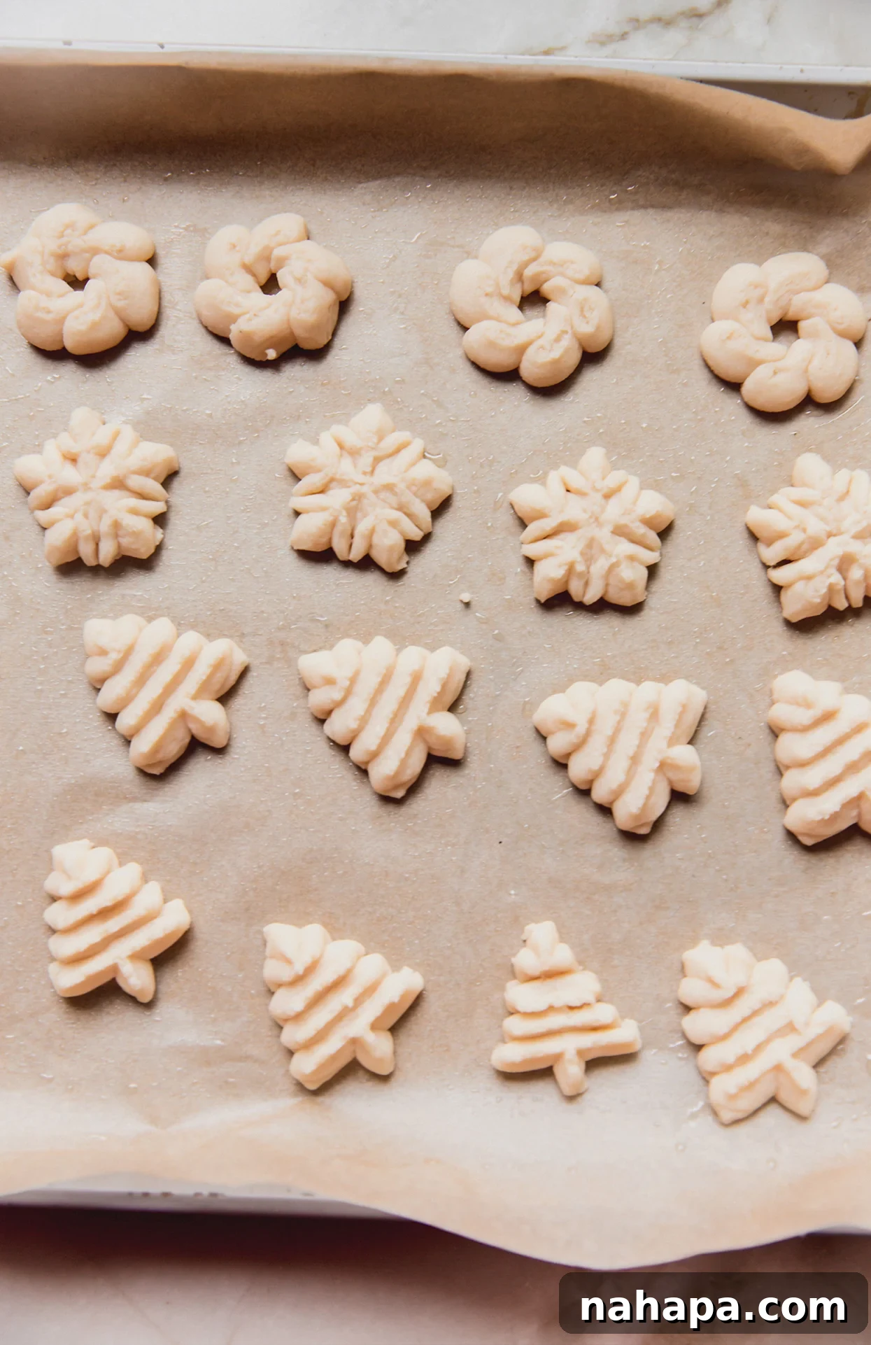 Unbaked spritz cookies, beautifully formed into various festive shapes, arranged on a baking sheet.