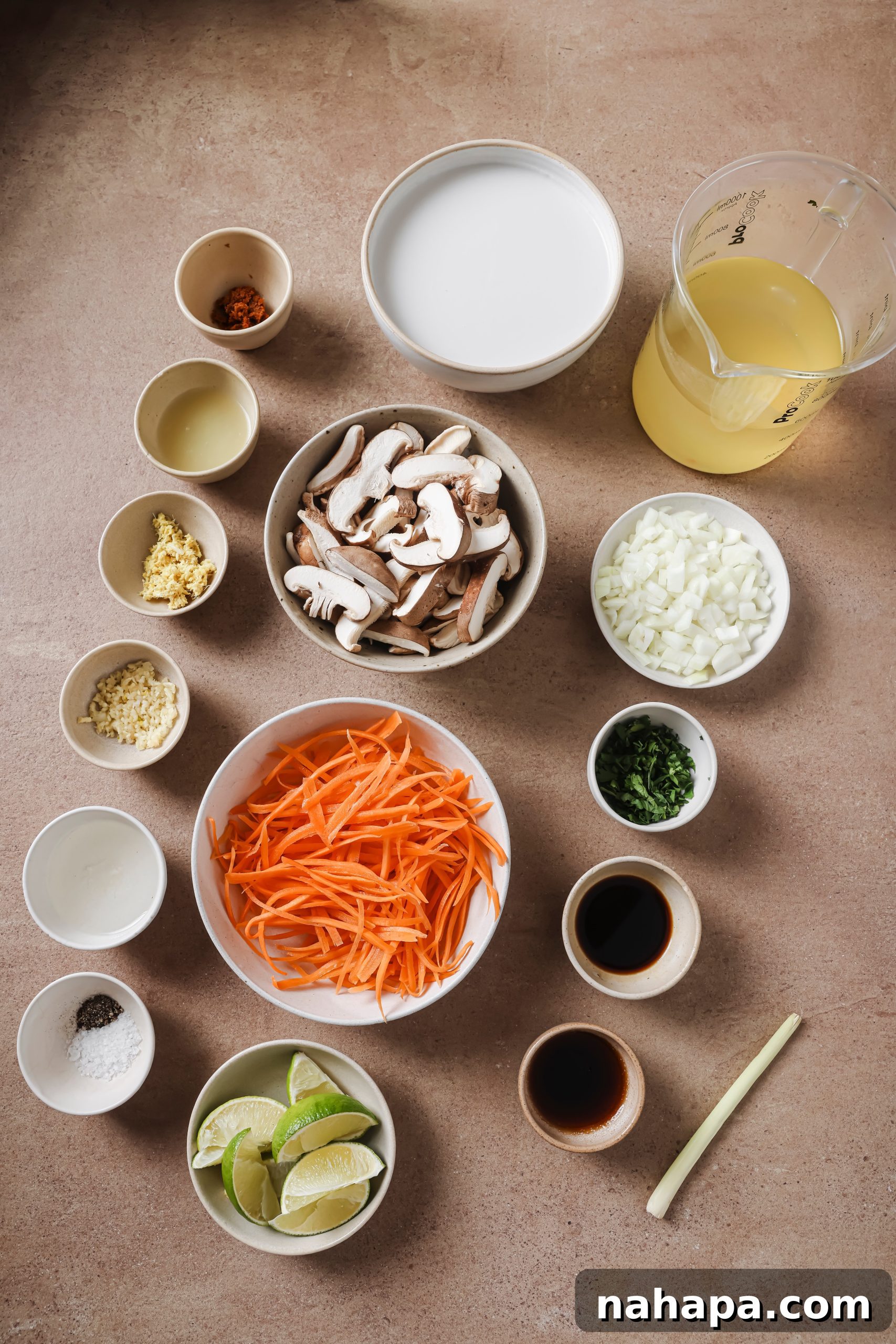 Various Tom Kha soup ingredients arranged artfully in small bowls, showcasing fresh shiitake mushrooms, carrots, ginger, garlic, and lime.