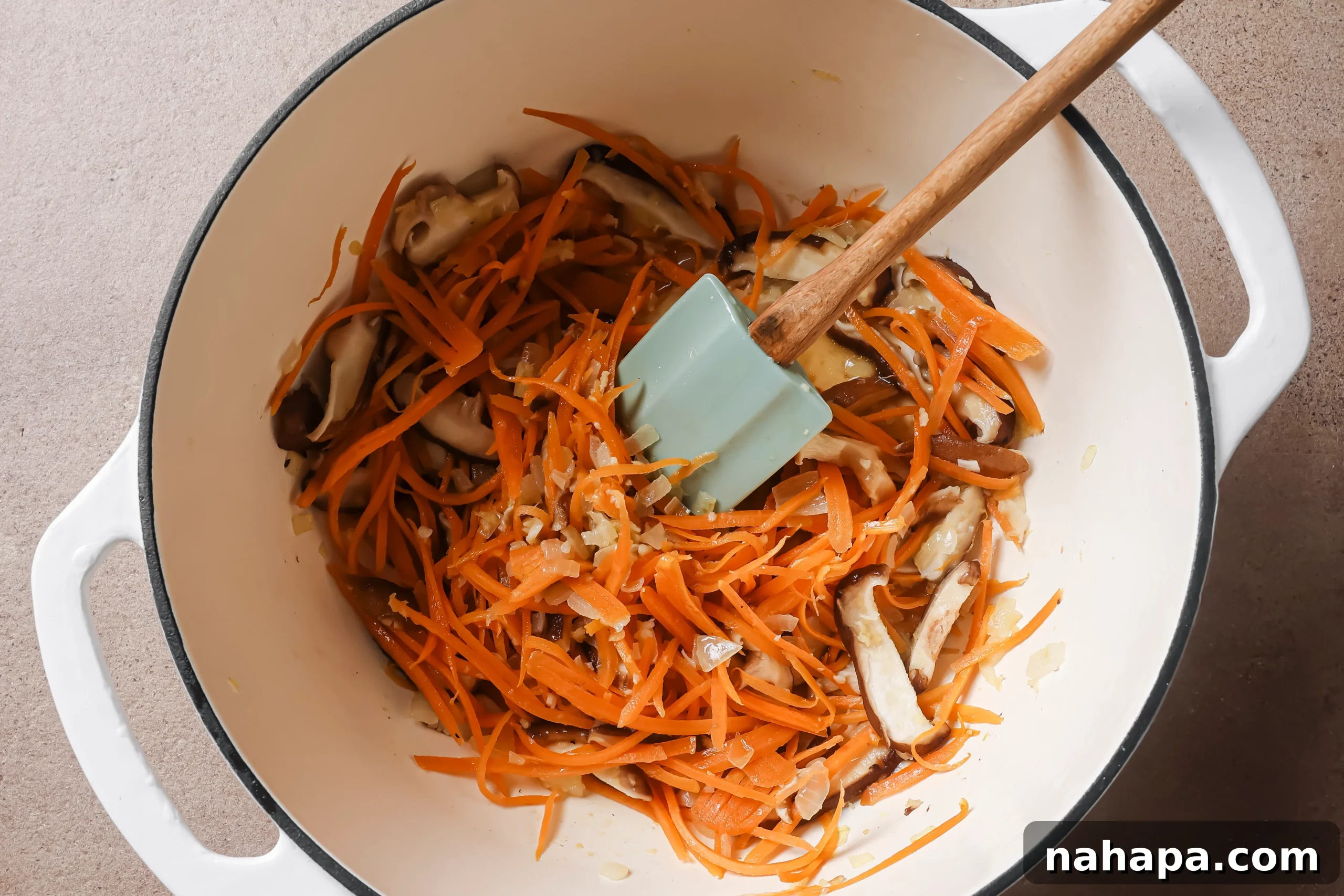A mix of onions, shredded carrots, and sliced shiitake mushrooms sautéing together in a pot, developing rich flavors and softening textures.