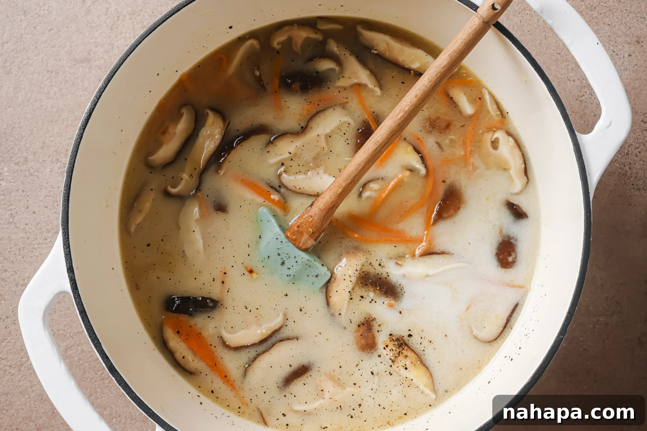 Broth, creamy coconut milk, and various seasonings being poured into a pot of sautéed vegetables, ready to be combined for Tom Kha soup.