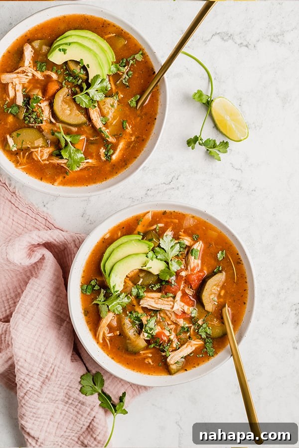 Two bowls of Instant Pot Chicken No-Tortilla Soup, richly garnished with avocado slices and fresh cilantro on a wooden surface.
