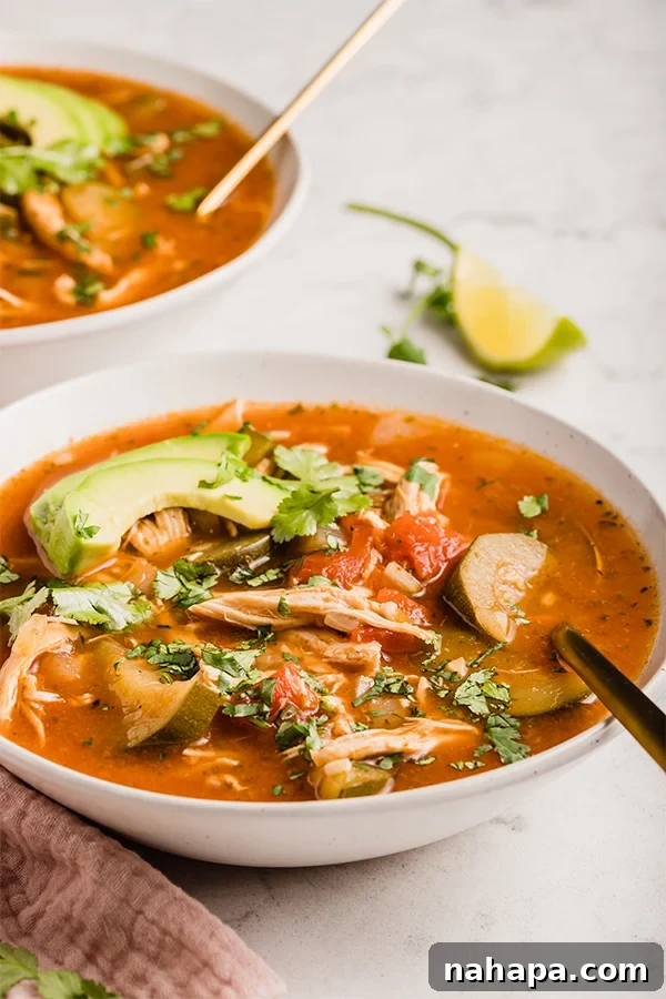 A close-up shot of Instant Pot Chicken No-Tortilla Soup in a bowl, showing the rich broth, shredded chicken, and zucchini, topped with fresh avocado.