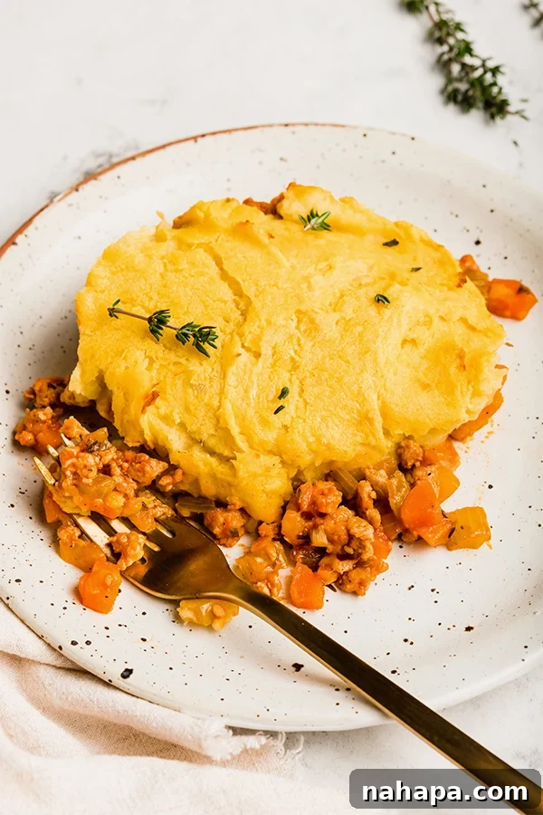 Ultimate Turkey Shepherds Bake 5 A serving of turkey shepherd's pie on a white plate, garnished with fresh herbs.