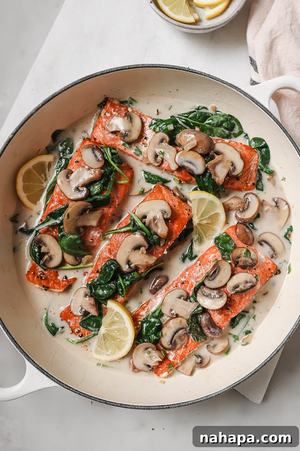 Creamy salmon Florentine topped with fresh lemon wedges, ready to serve in a large white pan.