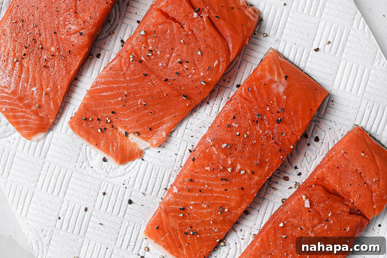 Raw salmon fillets, seasoned with salt and pepper, resting on a paper towel.