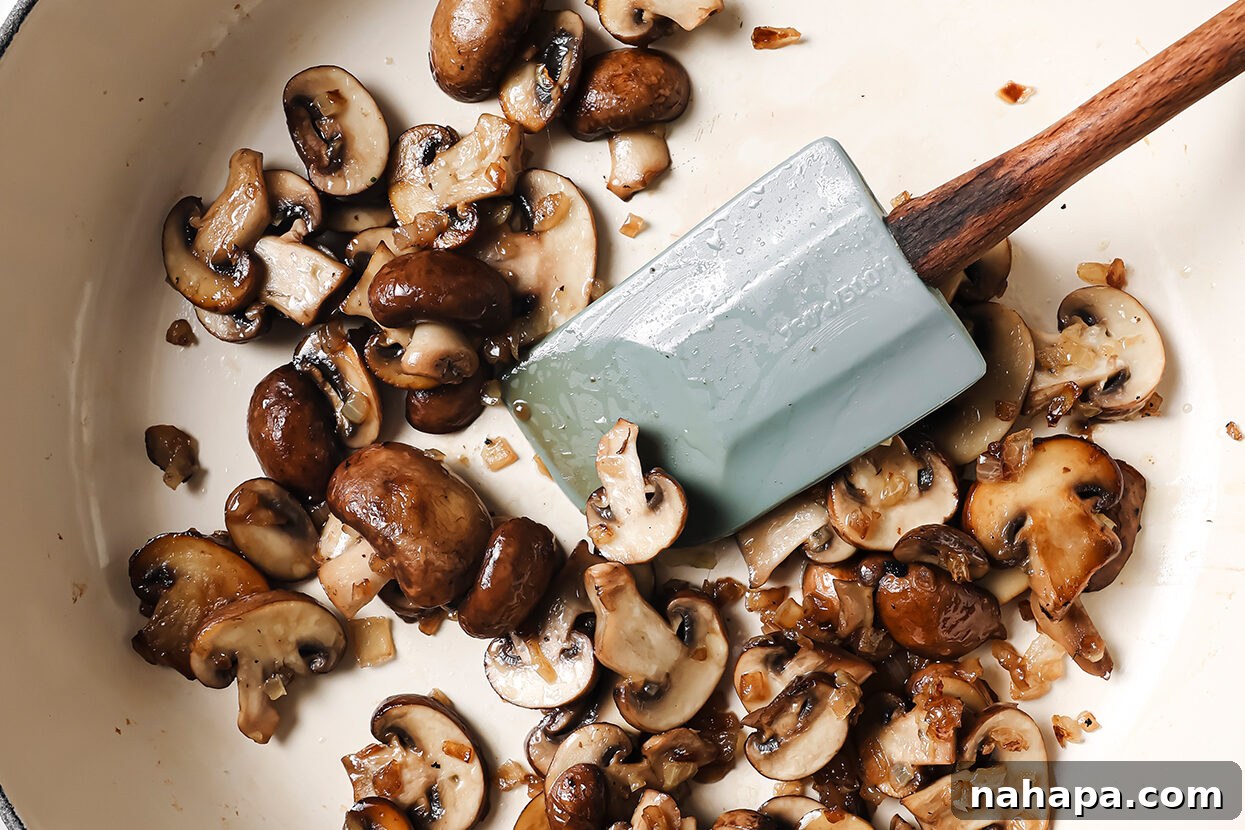 Sliced mushrooms being sautéed in a pan with a spatula until tender and golden brown.