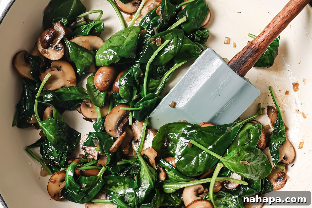 Mushrooms and fresh spinach being cooked in a pan with minced garlic, wilting down beautifully.