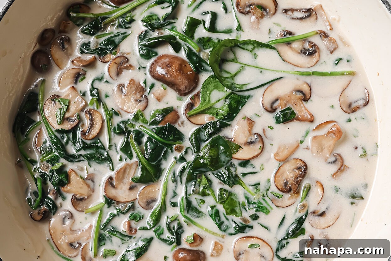 The creamy Florentine sauce, featuring mushrooms and spinach, simmering in a pan to thicken.