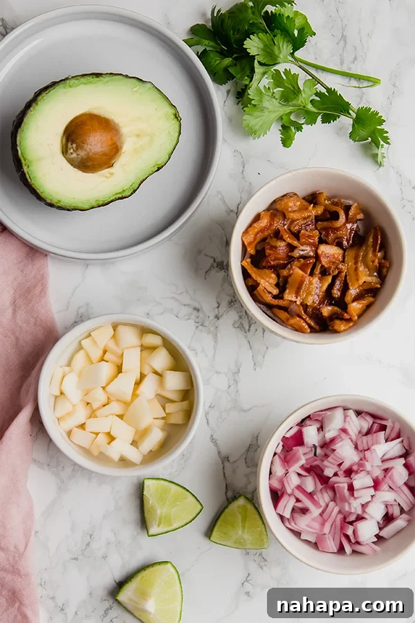 Applewood Bacon Guacamole 3 Assorted ingredients for Apple Bacon Guacamole laid out: fresh avocados, crispy bacon, sliced pink lady apple, lime, red onion, garlic, and avocado oil