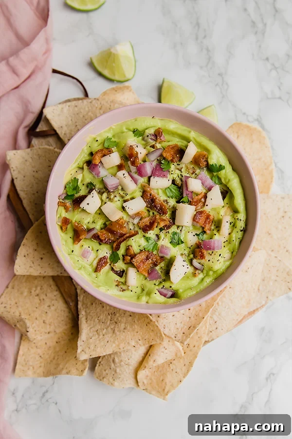 Applewood Bacon Guacamole 4 Close-up of Apple Bacon Guacamole in a bowl with a variety of dippers including plantain chips and fresh vegetables