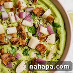 A bowl of Apple Bacon Guacamole with a spoon, ready to be served