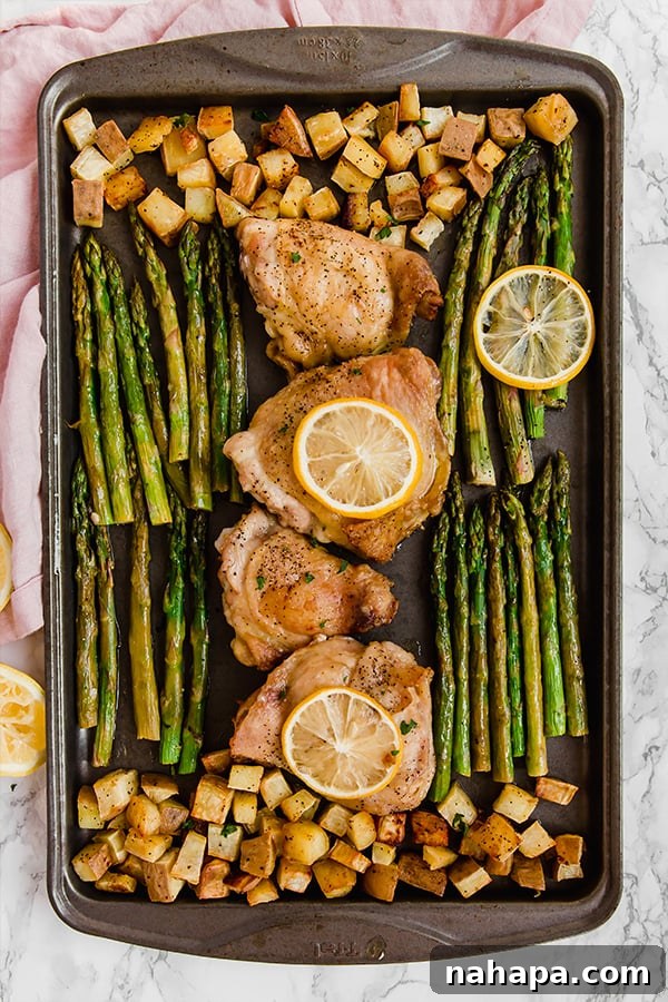 Effortless Lemon Garlic Chicken and Asparagus 3 Sheet pan with chicken thighs, sweet potatoes, and asparagus roasting in the oven
