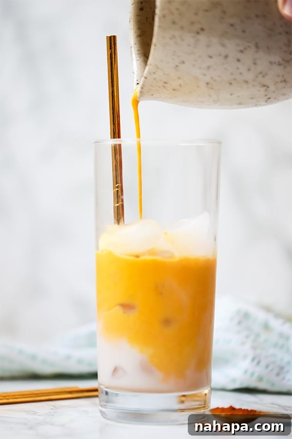 An iced golden milk turmeric latte in a clear glass with a straw, garnished with spices.