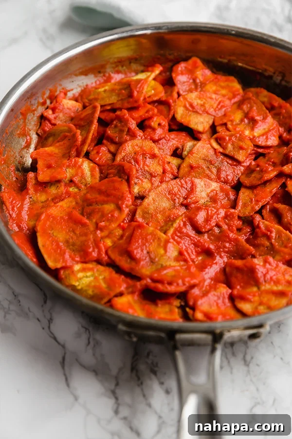 Plantain chips being coated in rich enchilada sauce in a skillet