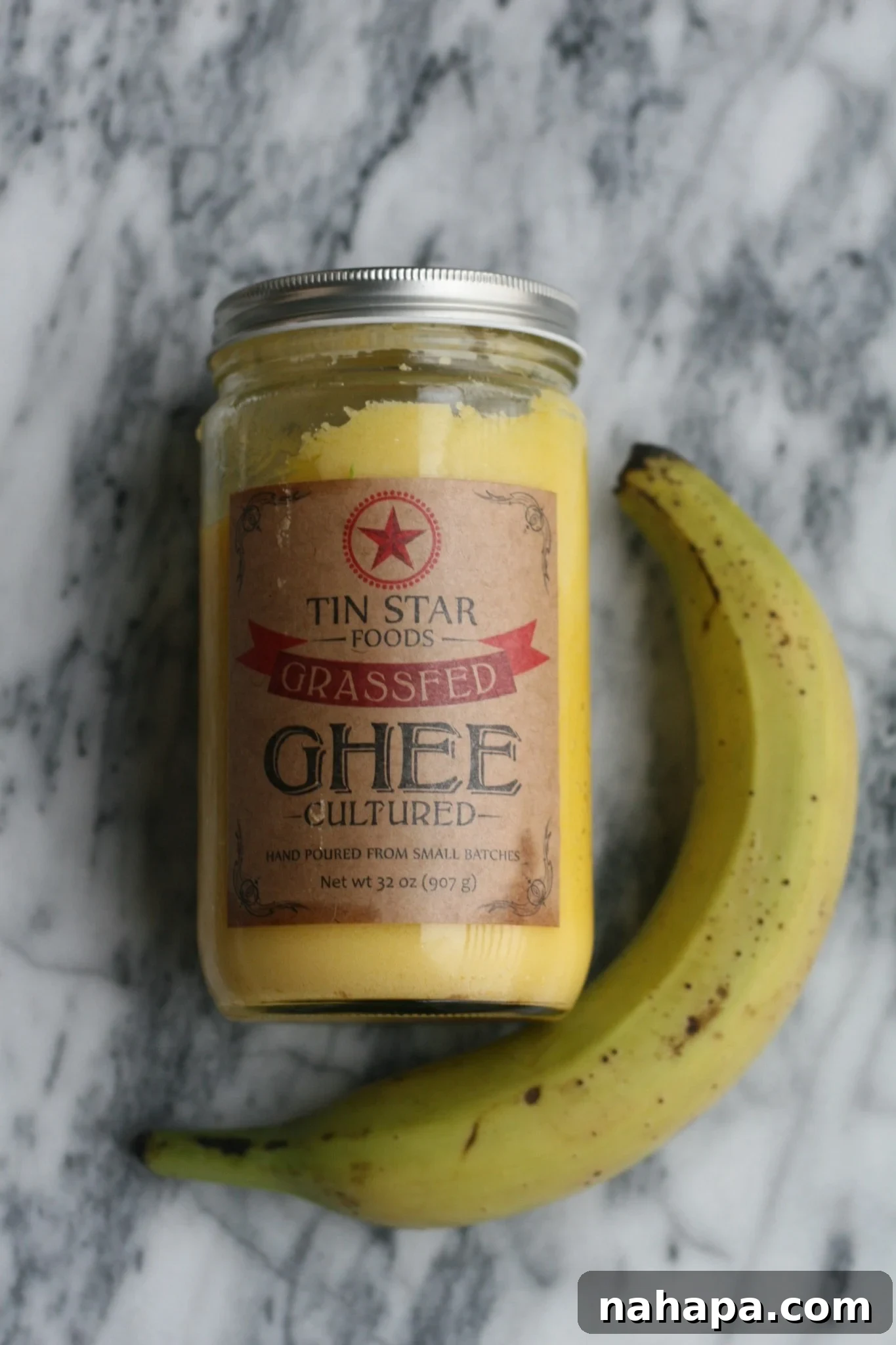 Autoimmune-Friendly Oven Baked Plantains 3 A jar of Tin Star Foods Ghee next to a green plantain on a kitchen counter, ready for cooking.