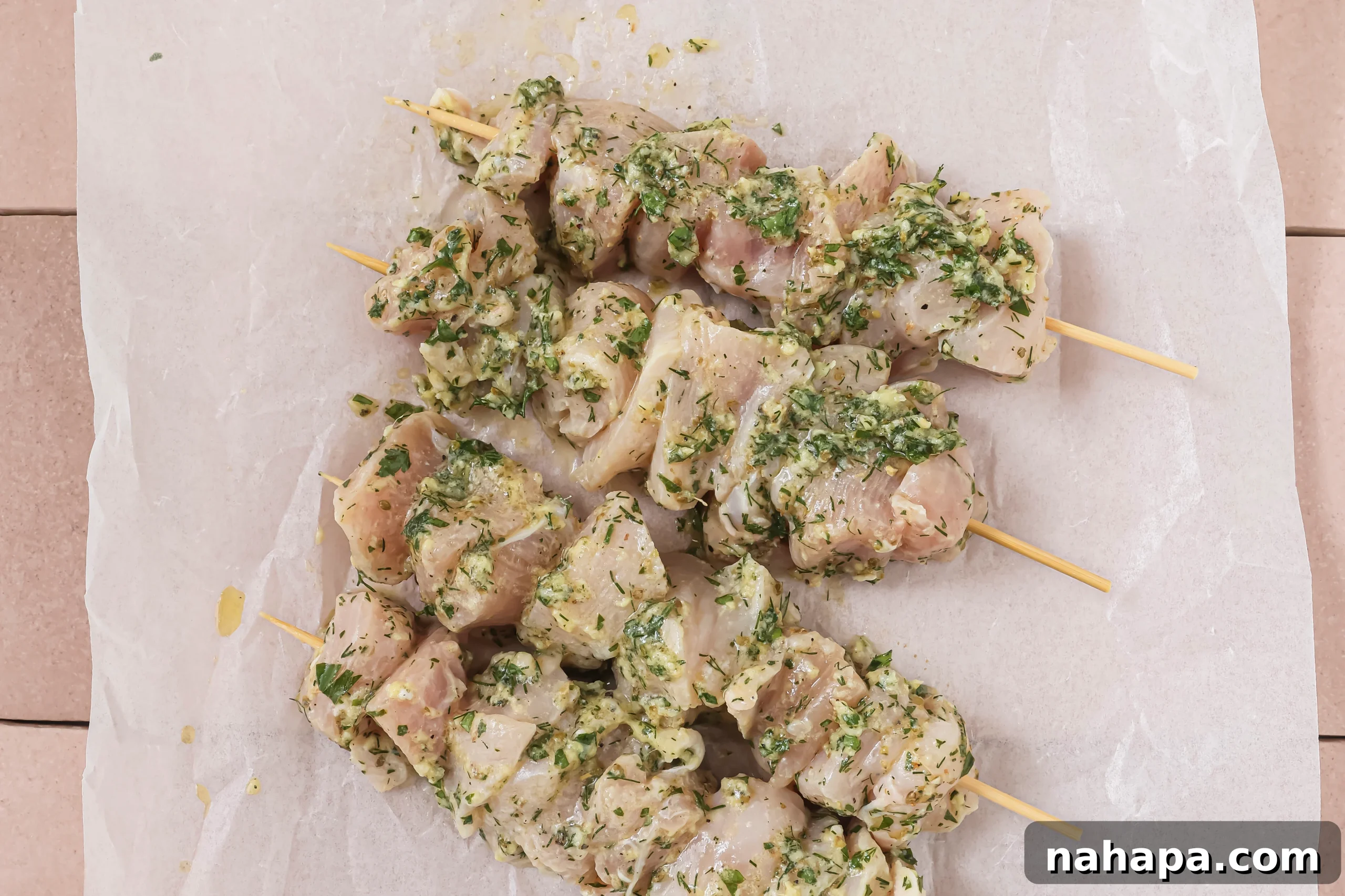Raw chicken breast cubes threaded onto wooden skewers, generously coated in a zesty Greek marinade, ready for grilling.