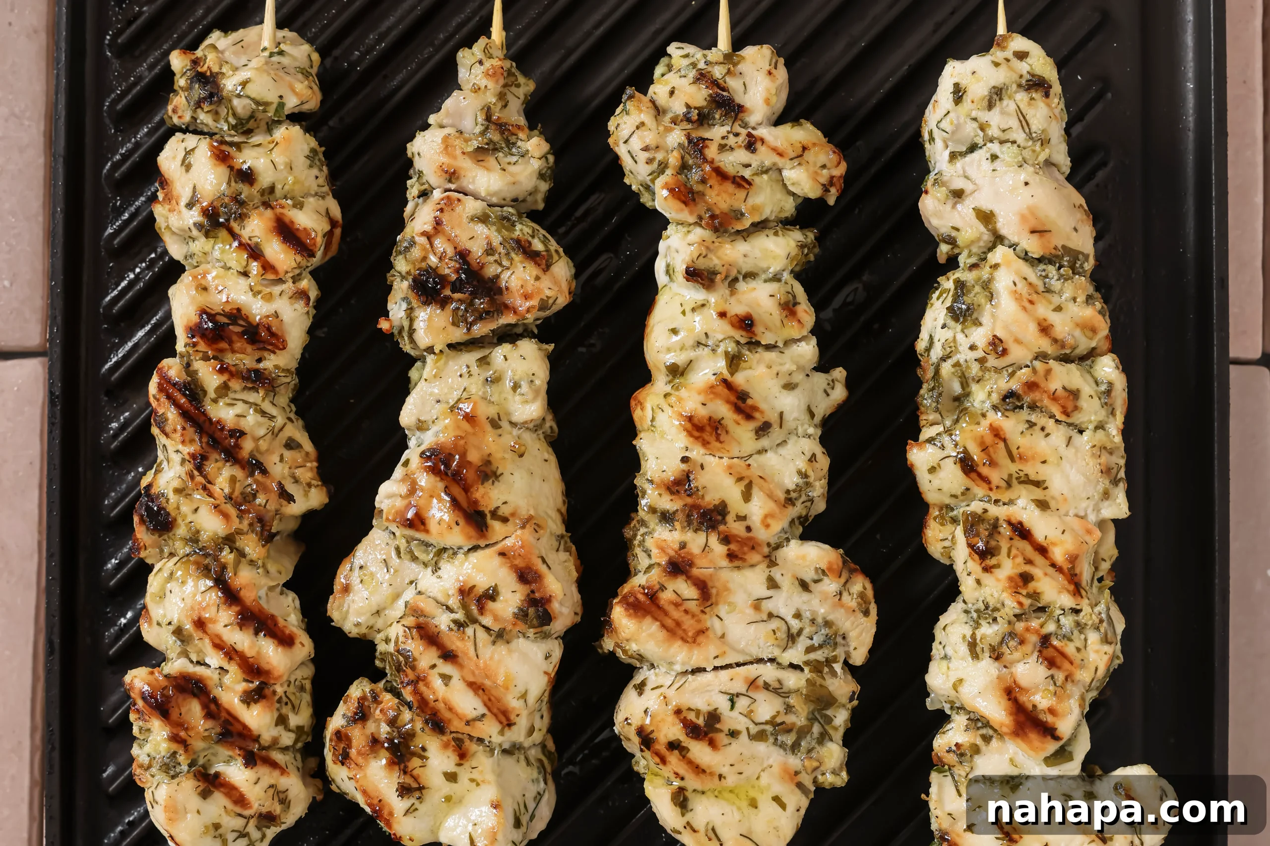 Chicken souvlaki skewers sizzling on a hot indoor cast iron grill pan, developing beautiful char marks and cooking evenly.