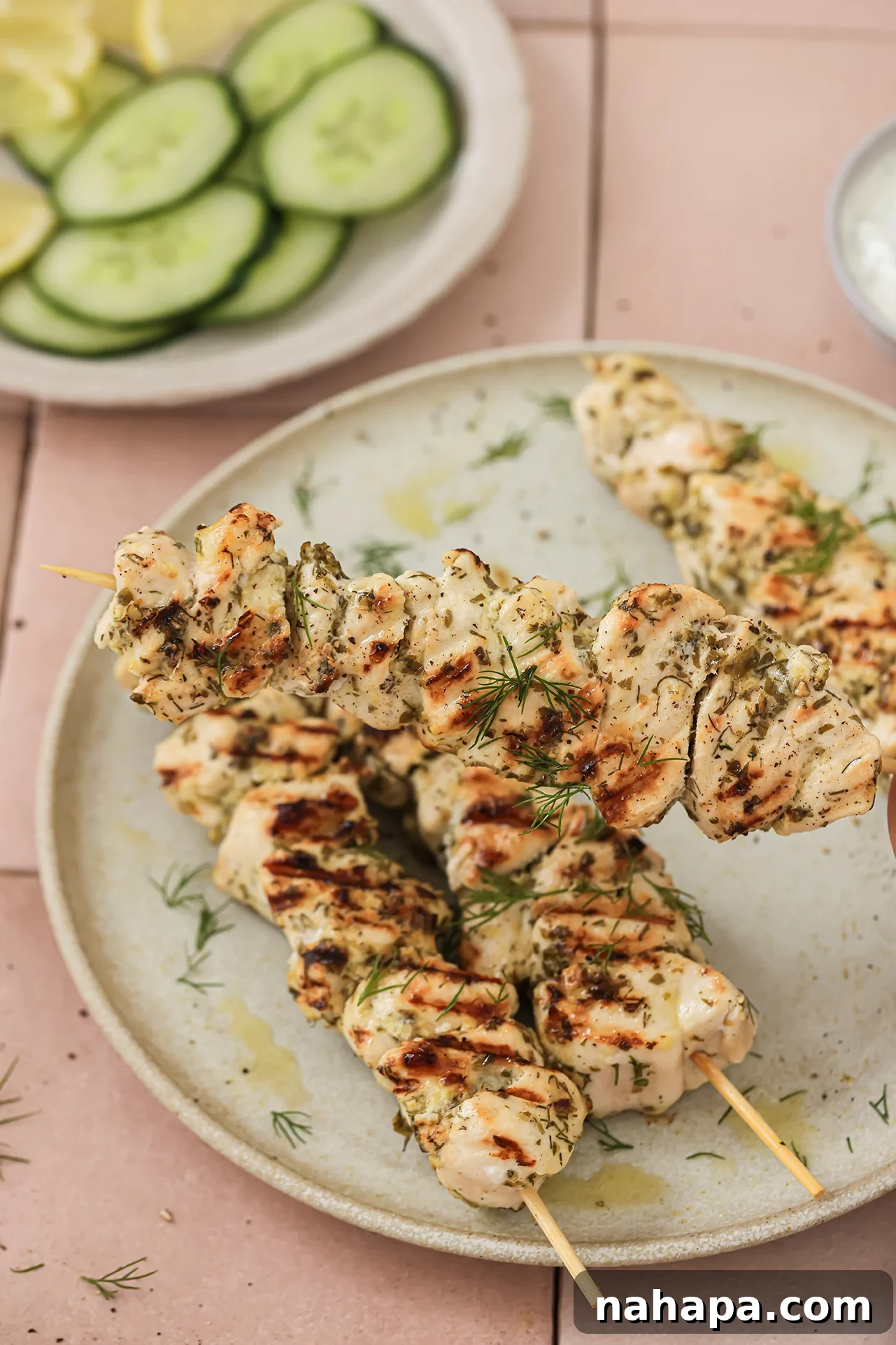 A hand reaching for a perfectly grilled chicken souvlaki skewer from a platter, highlighting the delicious texture and inviting presentation.