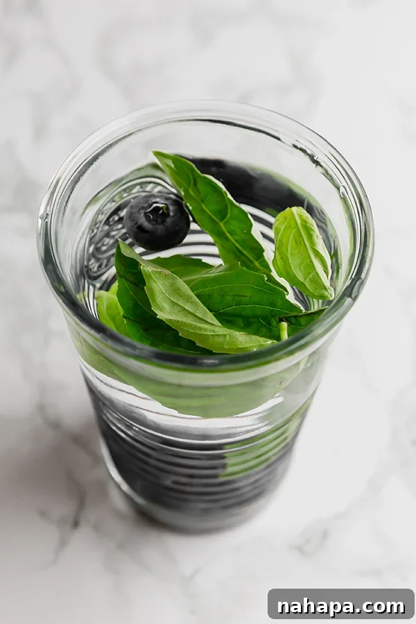 A top-down view of several infused water glasses arranged on a table with fresh fruits and herbs scattered around them.