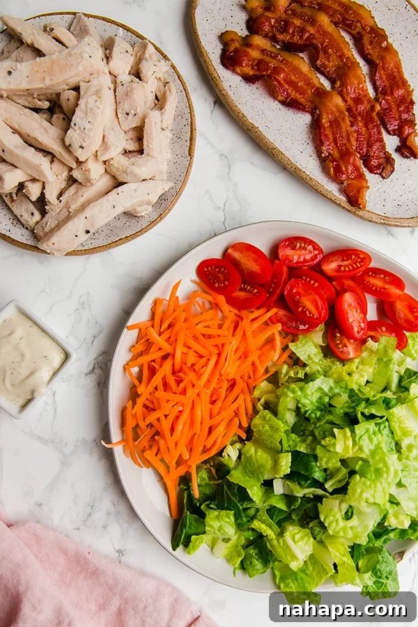 Ingredients for Paleo Chicken Bacon Ranch Wraps laid out: cooked chicken, crispy bacon, ranch dressing, lettuce, carrots, and Siete tortillas.