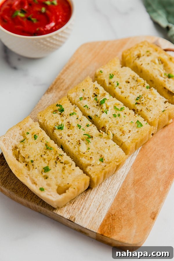 Deliciously golden-brown gluten-free garlic bread slices resting on a wooden cutting board, garnished with fresh parsley, with a side of rich marinara sauce in a small bowl.