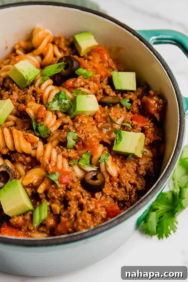 Close-up of paleo taco pasta simmering in a large pot, with ground beef, fusilli pasta, and a rich, red sauce visible.