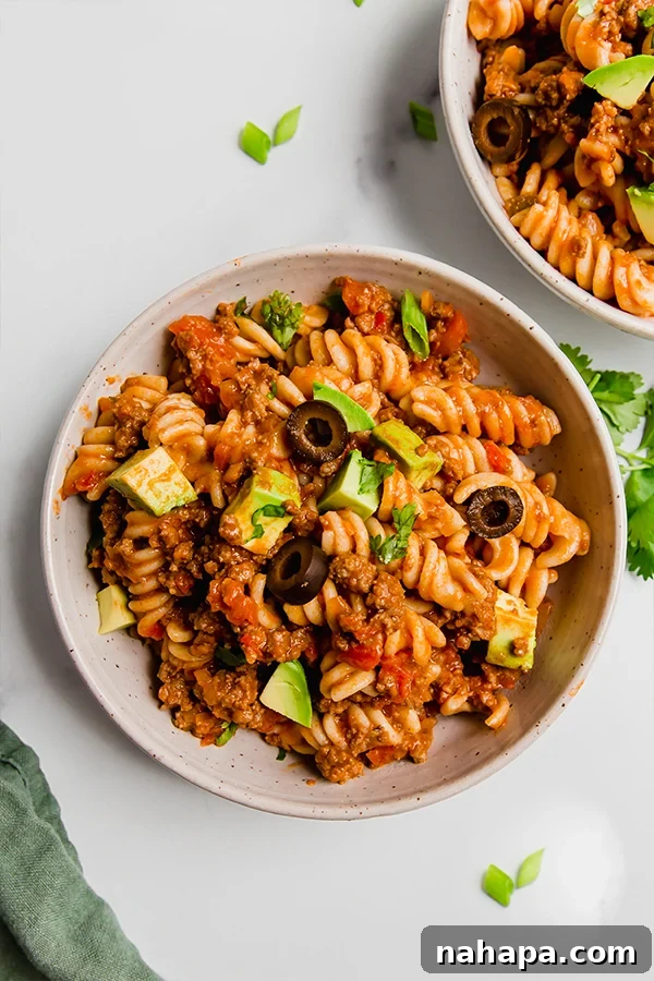 A serving of One-Pot Paleo Taco Pasta in a bowl, topped with avocado slices, fresh cilantro, and a lime wedge. The rich, textured pasta is prominent.