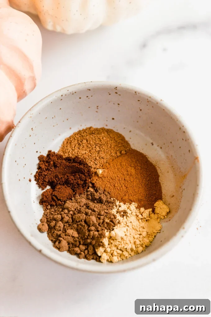 A close-up shot of a small bowl filled with homemade chai pumpkin spice blend, featuring ground ginger, cinnamon, cloves, and nutmeg, ready for a delicious latte.