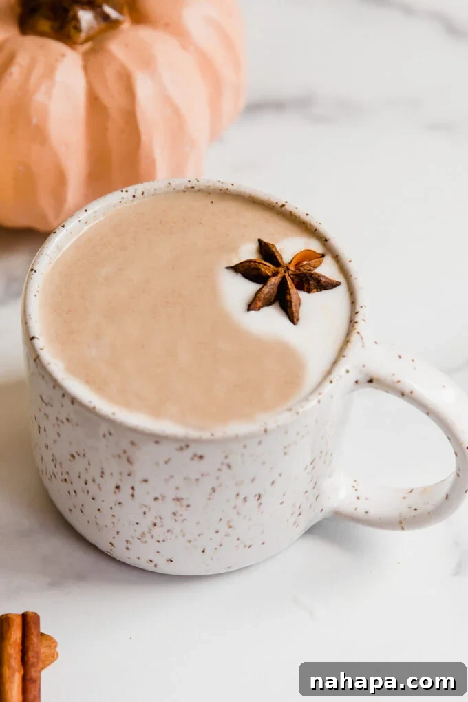 A warm Chai Pumpkin Spice Latte in a rustic mug, with a decorative pumpkin in the soft background, evoking a cozy fall atmosphere. Dairy-free, Paleo, and AIP-friendly.