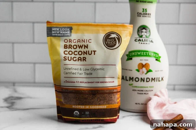 Ingredients for a Snickerdoodle Latte artfully arranged on a rustic wooden surface, including almond milk, cinnamon, coconut sugar, and coffee beans.