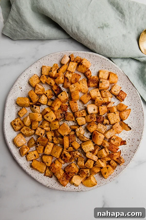 A vibrant close-up of perfectly roasted rutabaga cubes, garnished with fresh herbs, on a wooden surface.