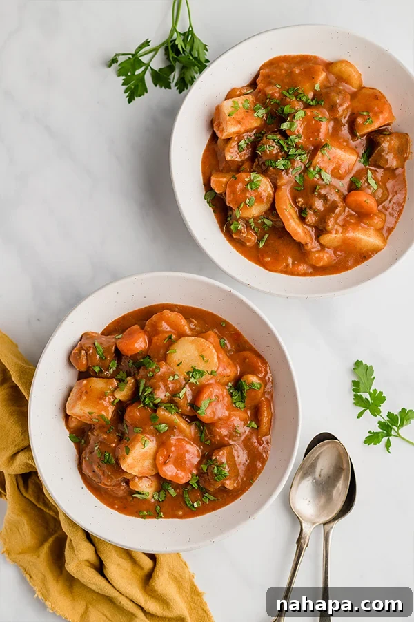 Two bowls of authentic Hungarian Goulash, garnished with parsley and sour cream, ready to be served.