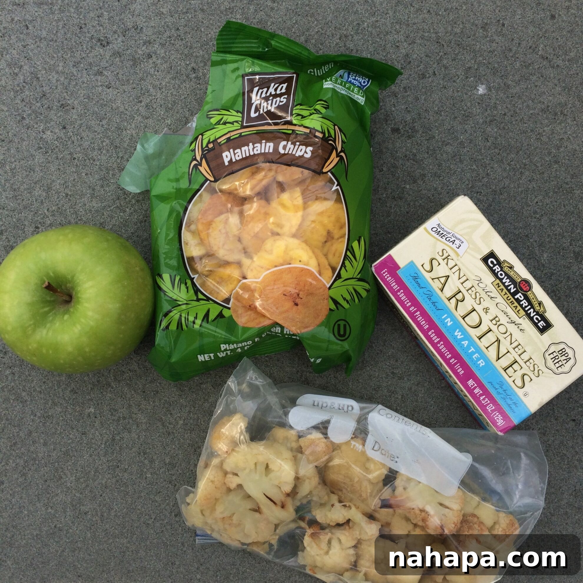 A delicious and colorful AIP-compliant lunch spread featuring crispy plantain chips, protein-rich sardines, tender roasted cauliflower, and a crisp apple, perfectly portioned for travel or a conference setting.