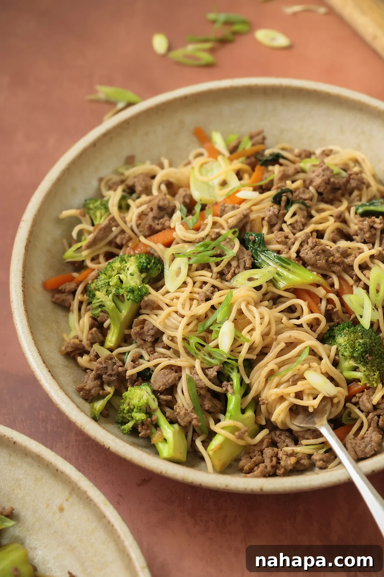 A vibrant bowl of ground beef ramen stir fry, garnished with fresh green onions, showcasing a delicious and healthy meal.