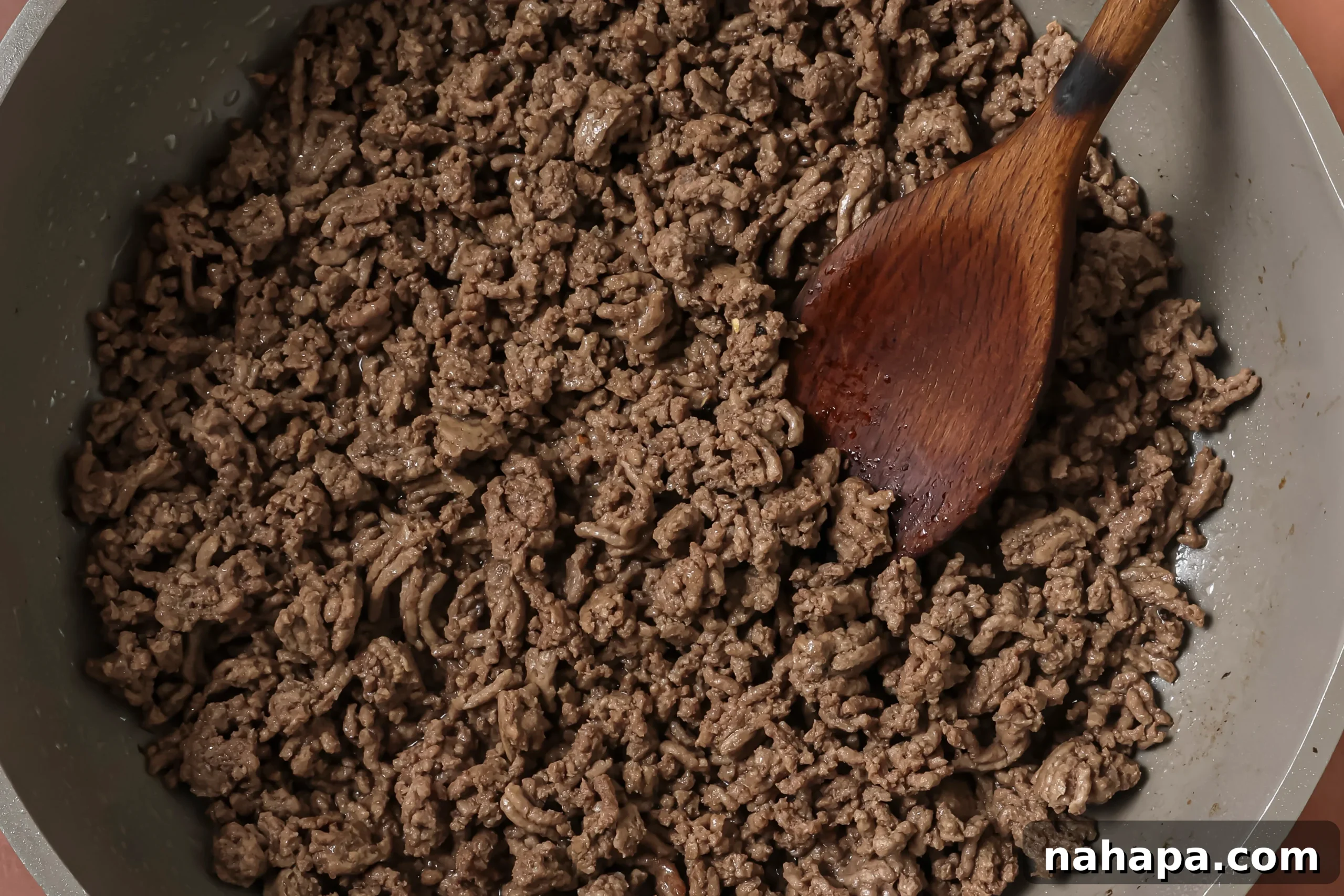 Browning ground beef in a large skillet with a wooden spoon, preparing it for the stir fry.