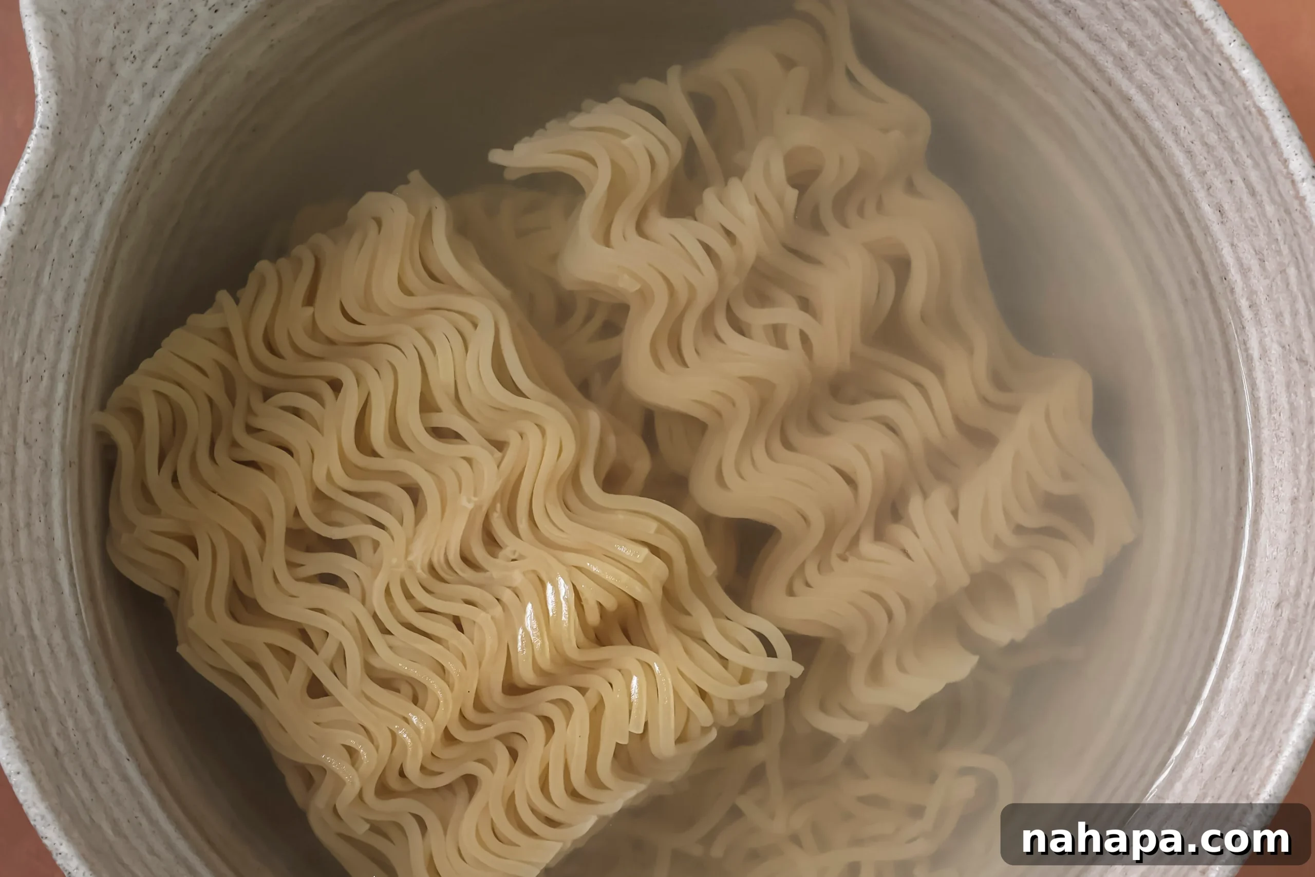 Gluten-free ramen noodles softening in a bowl of hot water, covered, as part of the preparation process.