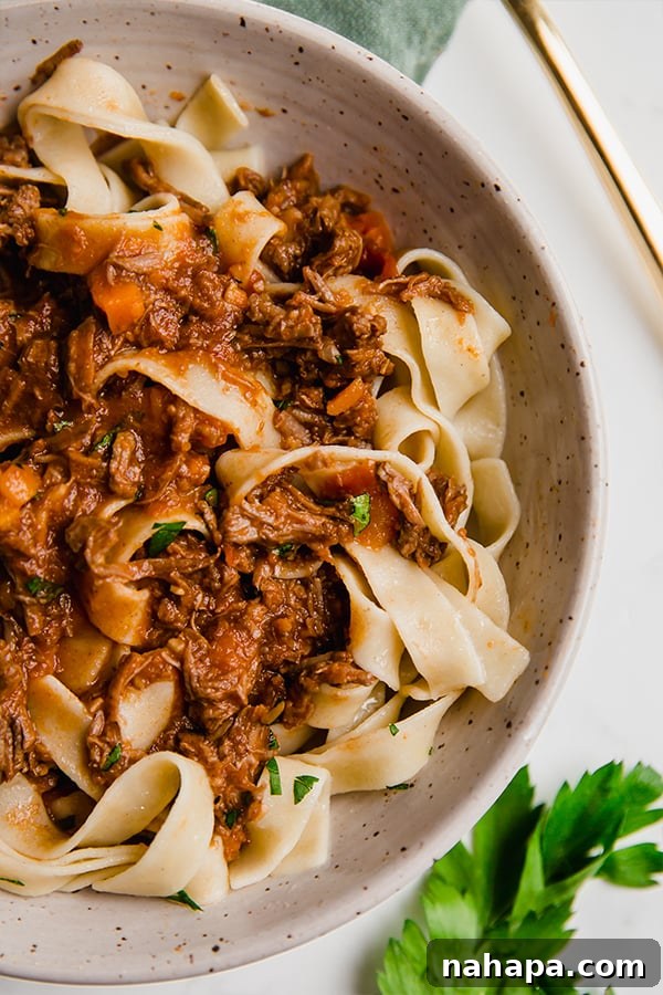 Rich slow cooker beef ragu served over pasta in a rustic bowl