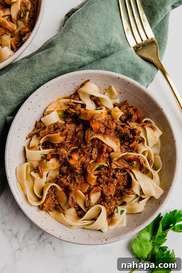 Two bowls of beef ragu with fresh parsley, served on a green cloth with a gold fork