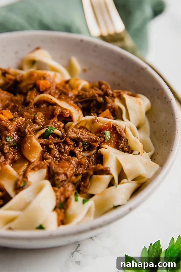 Close-up of slow cooker beef ragu in a serving bowl, garnished with fresh herbs