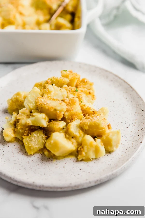 A serving of 'cheesy' sweet potato casserole on a plate, garnished with fresh herbs, showcasing its creamy texture.