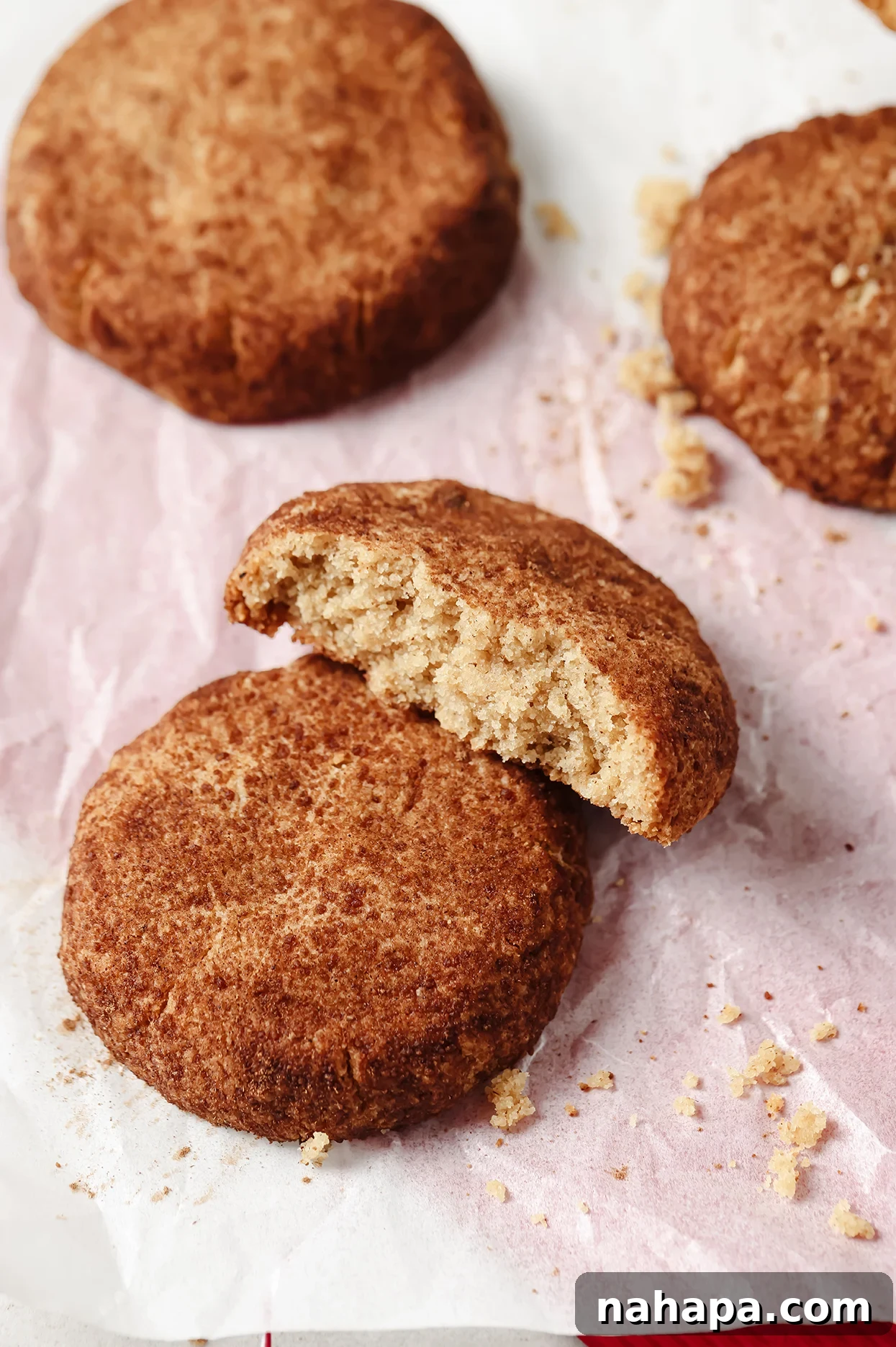 Freshly baked gluten-free Snickerdoodle cookies arranged on a baking tray, with one cookie gently broken in half to reveal its soft interior.