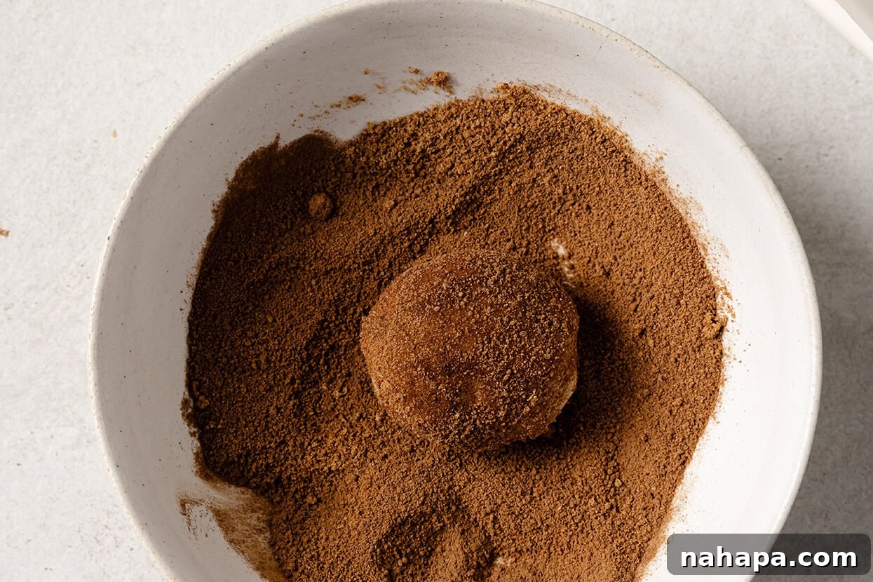 A ball of snickerdoodle dough being rolled in a bowl filled with the cinnamon-sugar mixture.